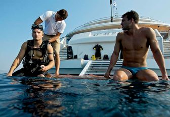 Two men sat on edge of O'MEGA superyacht with legs in water