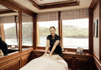 spa therapist gives guest a massage on motor yacht titania, with view of thailand in background