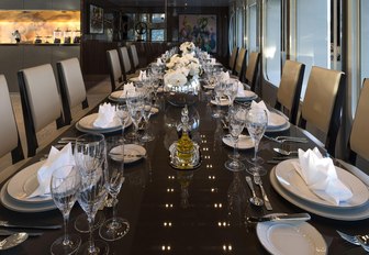 Formal dining arrangement onboard SERENITY, long dining table with elegant decor, with white upholstered chairs along either side