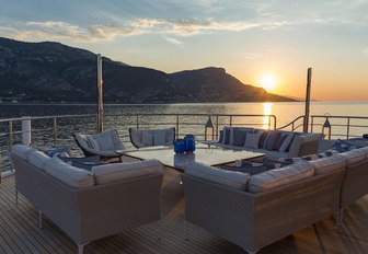 Aft deck exterior seating arrangement onboard M/Y SERENITY, overlooking elevated terrain and sunset over sea