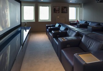 Indoor cinema room onboard 72m M/Y SERENITY, rows of plush leather chairs facing wall mounted screen.