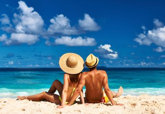 couple relax on white sand beach of the seychelles on their luxury yacht charter