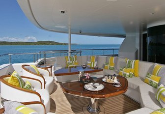 Aft deck onboard AMARYLLIS, white sofas and armchairs surround tables, surrounded by sea and distant islands.