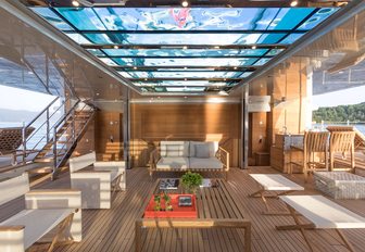 the spacious and airy beach club of crewed yacht lady lena illuminated by the glistening light that poors in through the glass bottom swimming pool that hovers over head and the extendeable side platforms on the side of the space