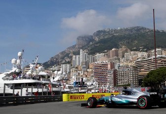A Mercedes Formula 1 car approaches the section of the race track lined with superyachts