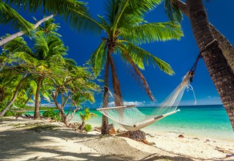 a hammock is tied up between two palm trees on a deserted, white sand beach in Fiji 