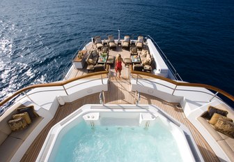 the spacious and glamorous main and upper aft decks of charter yacht utopia with a woman ascending the stairs from the spacious beach club to the jacuzzi