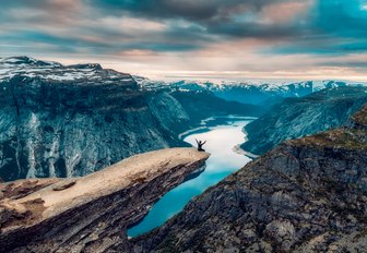 hiker sits on edge of Trolltunga Mountain in the Norwegian Fjords