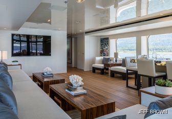 main salon on charter yacht chasseur, with light flooding in and wooden tables with white flowers on