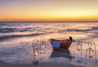 copper bath on the beach on thanda island, surrounded by candles with sun setting on horizon