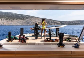 Water toys laid out on the swim platform with a charter guest looking out to sea onboard superyacht charter FLYING FOX