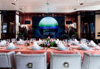 Formal dining salon on luxury charter yacht HEMILEA, with peach tablecloth and green and blue artwork in centre of wall