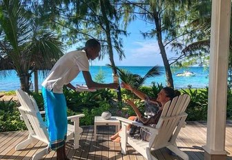 man serves woman drink on outdoor terrace of thanda island, a private island retreat off the coast of tanzania, with views over the ocean through palm trees in background