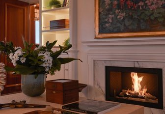 Fireplace on board luxury yacht Haida 1929, with oil paining hanging above and vase of flowers on coffee table