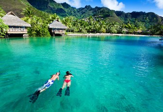 a couple snorkel in the beautiful, clear waters of Tahiti while on a charter vacation