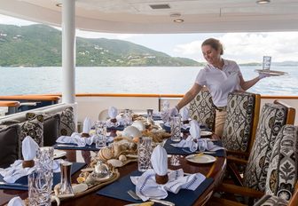 crew member sets up the aft deck dining area for a formal dinner aboard charter yacht BACCHUS 