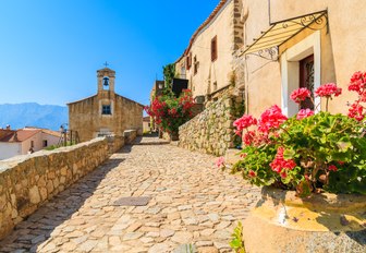 Cobbled streets in town of Corsica, with pink flowers and little stone chapel