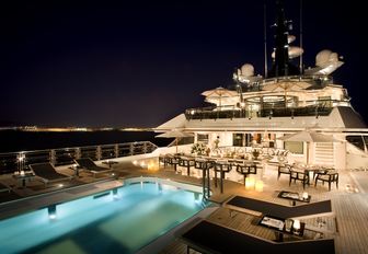 Upper deck of superyacht ALFA NERO, with large pool, bar area and social seating space lit-up at night