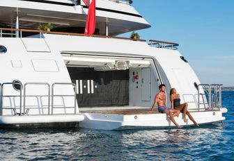 charter guests relax by the water's edge on drop-down swim platform aboard charter yacht 11-11
