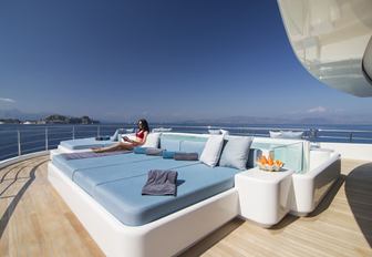 charter guest relaxes on a sun pad that surrounds the pool on board motor yacht O’PTASIA
