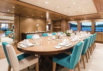large oval dining table with teak chairs in the main salon of luxury yacht Ramble on Rose 