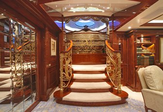Ornate central staircase on superyacht St David, with gold plating, gleaming wood and white carpets