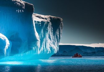 a RIB explores the dramatic ice-carved coastline of Antarctica as the sun sets