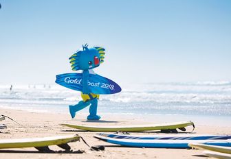 Borobi, the mascot for Gold Coast 2018, walks on Gold Coast beach with surfboard