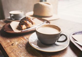 A wooden table laid with a milky coffee and a croissant