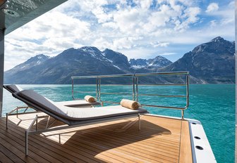 A sunlounger on a superyacht balcony faces out towards a mountainous landscape