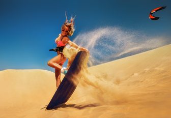 A woman performs a nose grab whilst sand surfing down a dune
