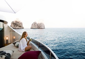 guest relaxes with a drink on the master suite balcony aboard luxury yacht QUITE ESSENTIAL