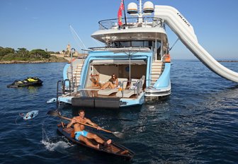 guest relaxes on the drop-down swim platform of motor yacht AURELIA as another guest kayaks past
