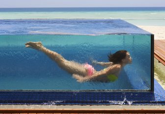 A woman swims underwater in a glass infinity pool on Thanda Island, Indian Ocean