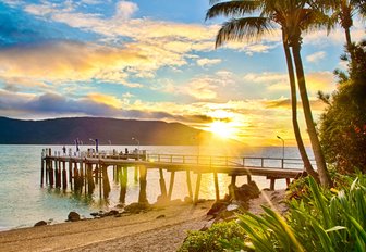 sun sets over the horizon on beach with wooden pier in the Whitsunday Islands