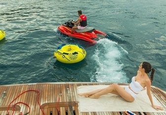 female guest relaxes on the swim platform as male guest tries out the jet ski on board motor yacht THEORIS 