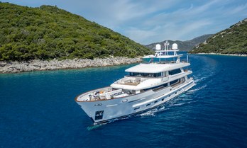 Charter yacht SUNRISE underway, with elevated lush green terrain on either side