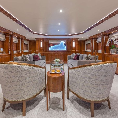 Overview of the main salon onboard charter yacht ARIADNE. Grey seating facing inwards with wooden shelving and decor around the walls.