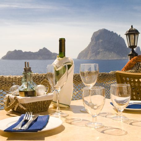 A bottle of wine and lunch plate settings on a table overlooking the coast of Ibiza