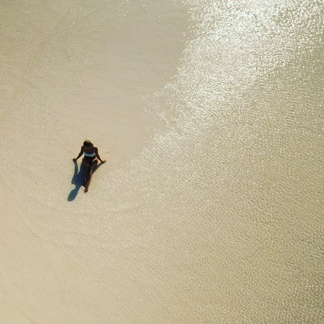 Aerial shot of a girl sat in her bikini in the shallow water 