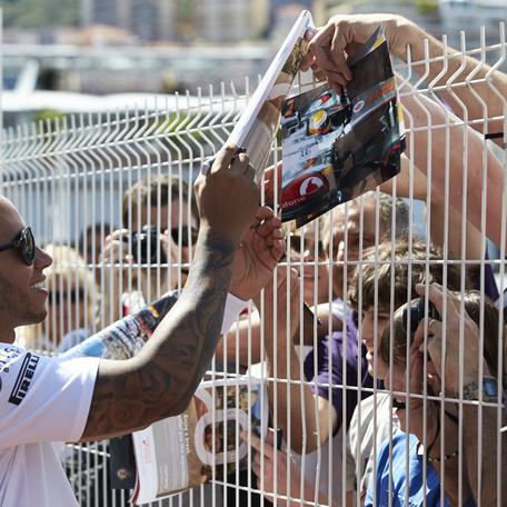 Lewis Hamilton signing autographs through a white fence at the Monaco Grand Prix