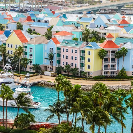 Hotels with colored roofs in the Bahamas with a motor yacht cruising by some palm trees in the foreground