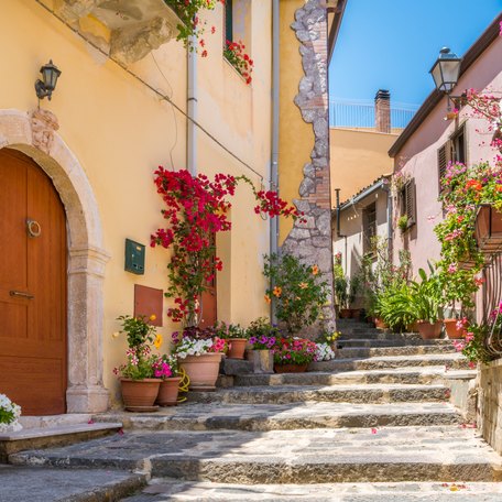 A narrow, cobbled, Italian street with floral arrangements either side