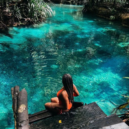 Girl in orange bikini sat on a jetty over the river's blue waters 