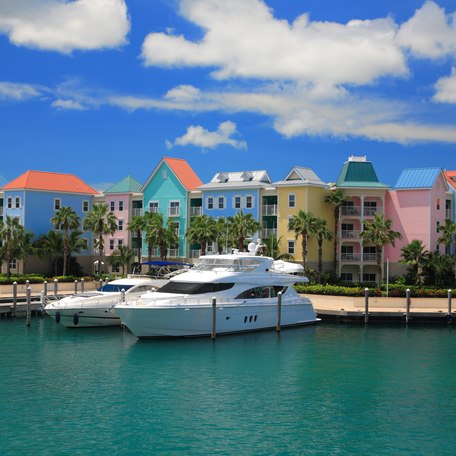 Motor yachts berthed in a small marina in front of colored Bahamian buildings