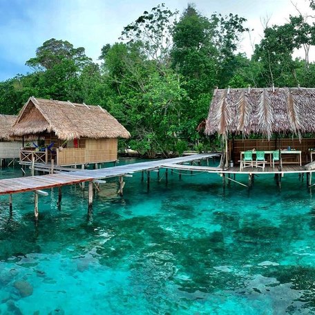 Three homestays on either side of small wooden pier of turquoise blue water 