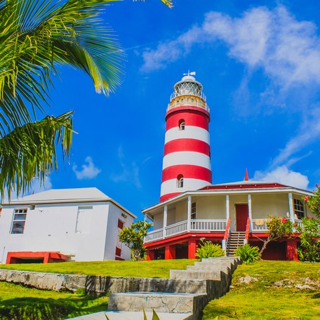 Ground view of a candy striped lighthouse in the Bahamas, with other red and white buildings in the foreground