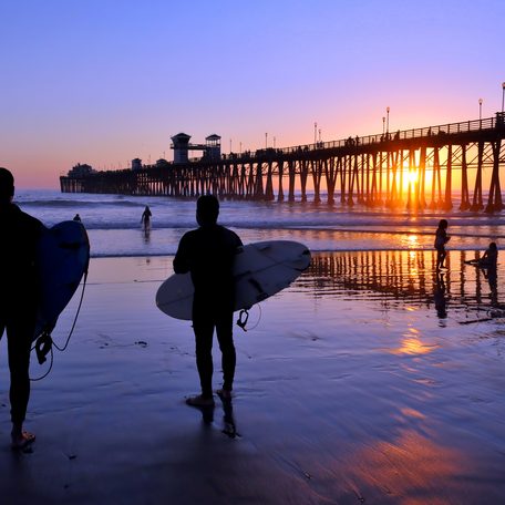 Two charter guests with surfboards walking on a beach at sunset