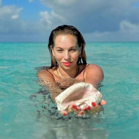 Woman in the water holding up conch shell 
