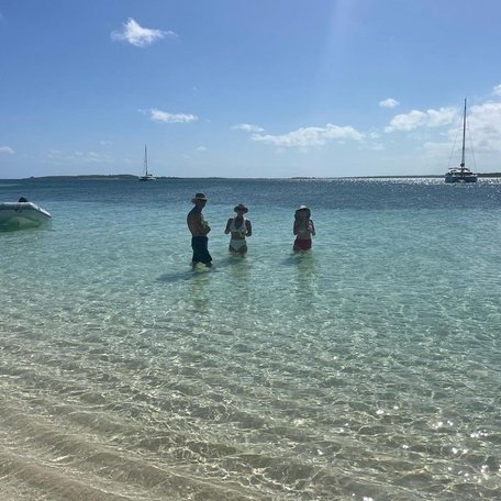 Family standing in the water by the shoreline with yachts in the distance 